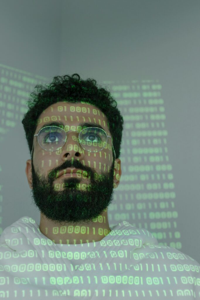 pexels-photo-5474028-5474028 A bearded man with eyeglasses analyzing data in a digital environment with green binary code projections.