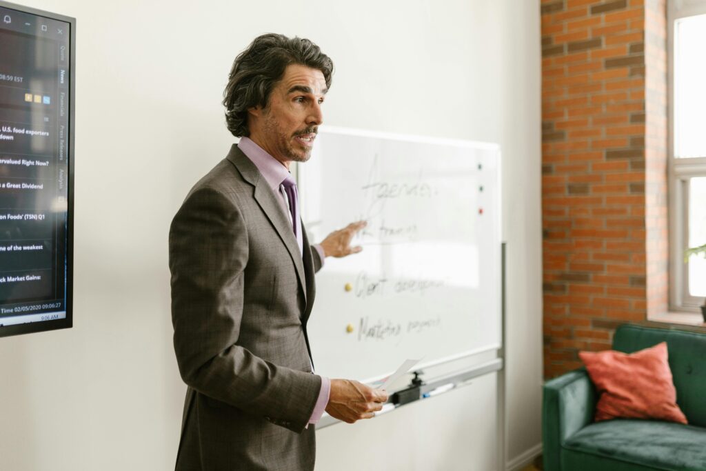 pexels-photo-8123796-8123796 Professional businessman explaining strategy during meeting using a whiteboard in a modern office setting.